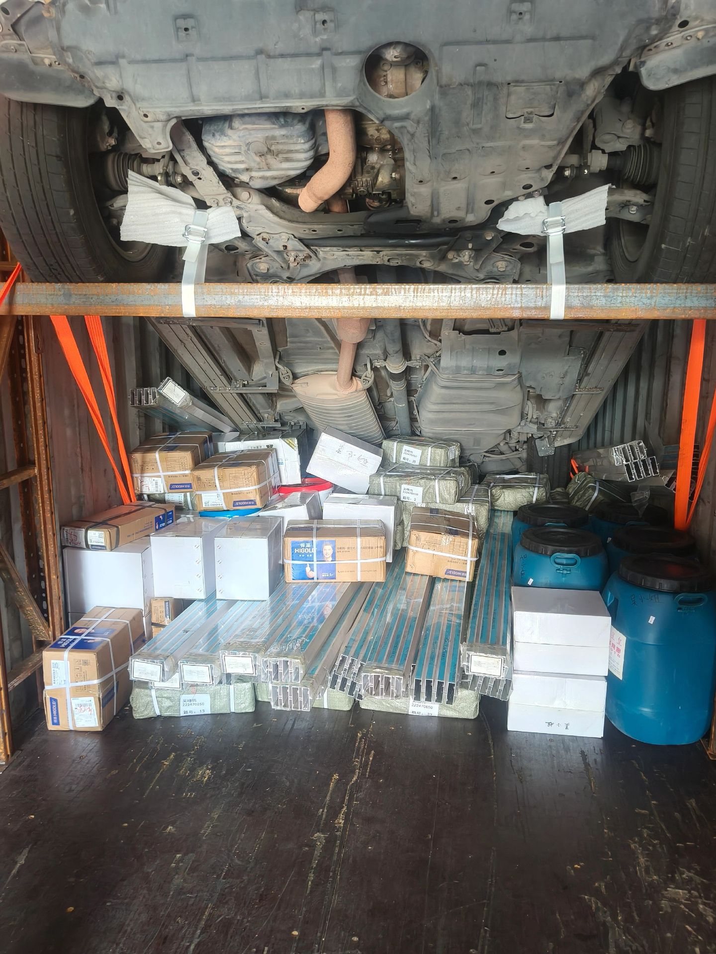 Inside a shared container: a passenger car racked on the upper level above general cargo, strapped to the walls