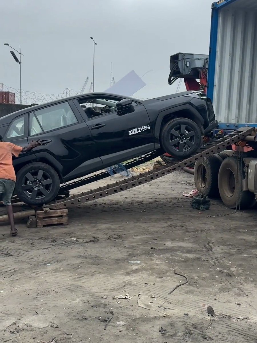 A worker guiding a black RAV4 down wooden ramps during container discharge