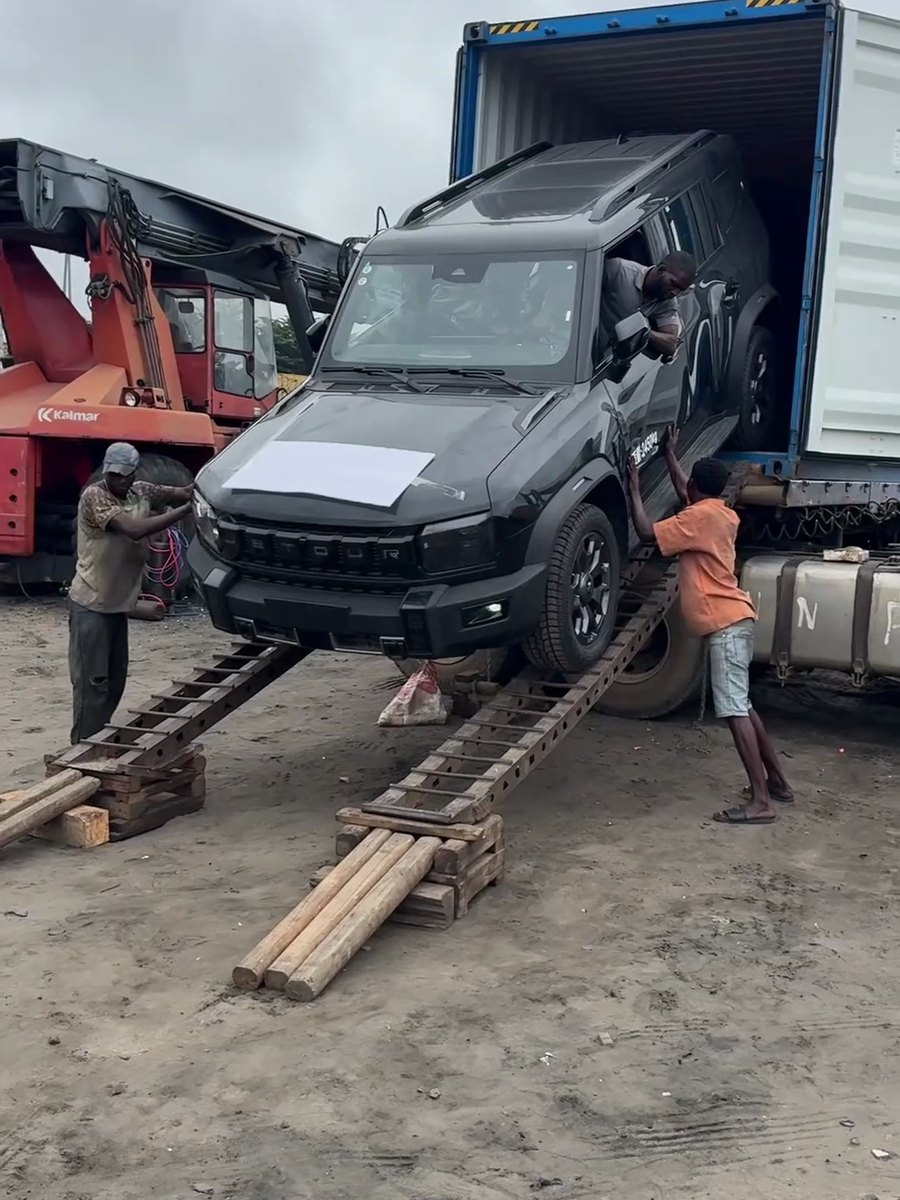 A dark SUV on wooden ramps at a container door, workers guiding and a Kalmar forklift nearby