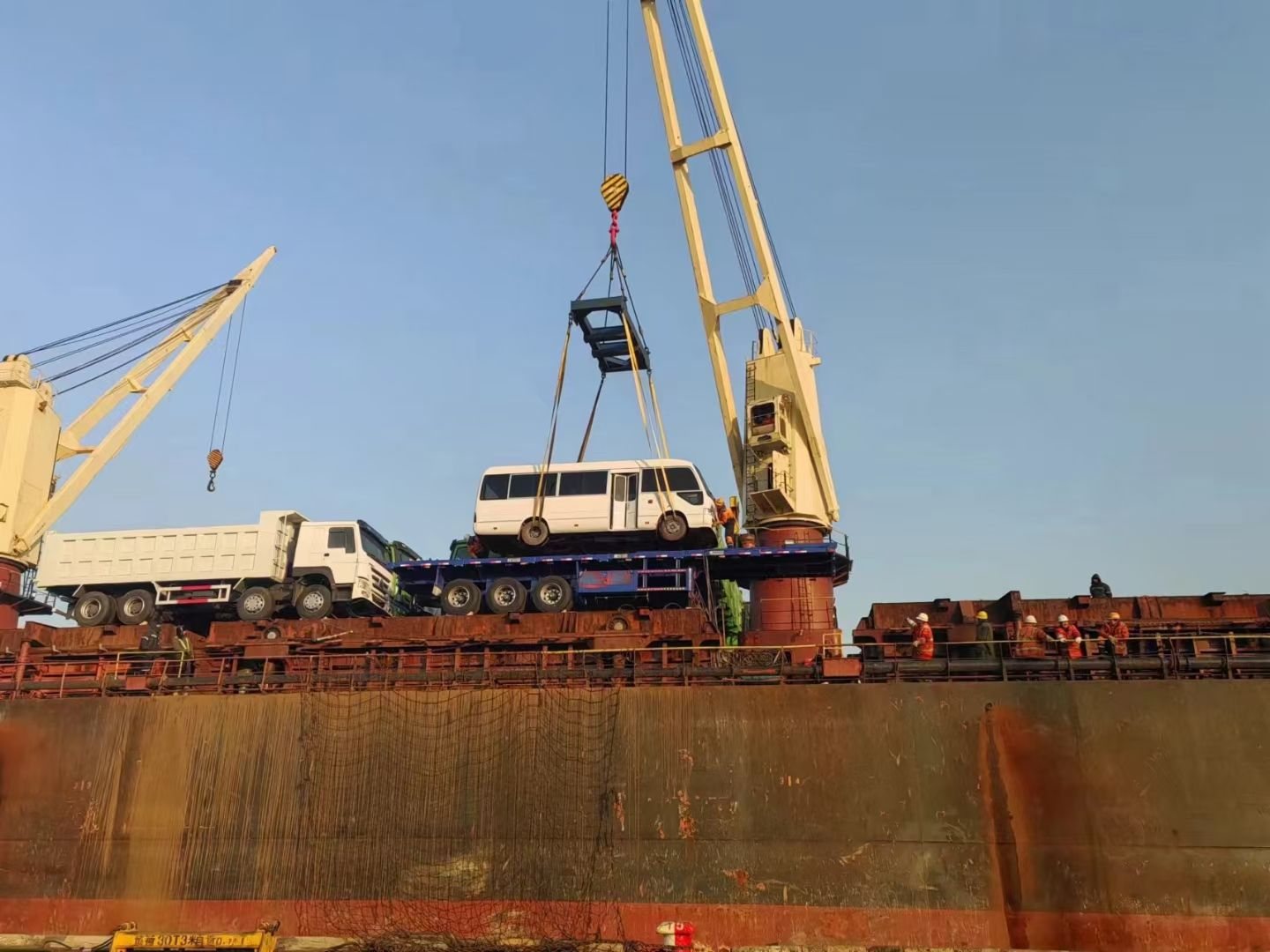 A passenger bus lifted by the ship crane onto a flatbed on a breakbulk vessel deck