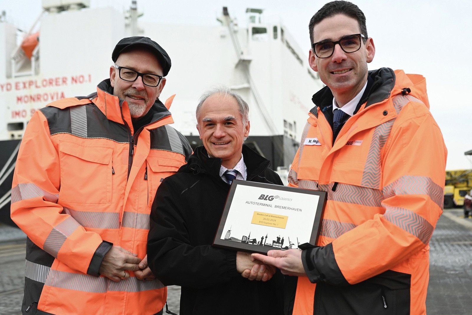 Terminal staff in high-visibility jackets with a pure car and truck carrier berthed behind them