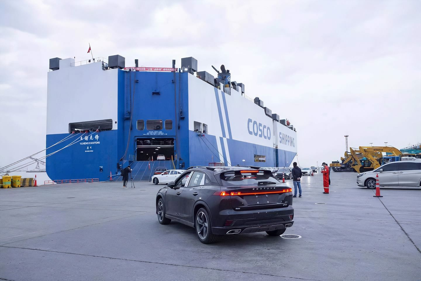 New energy vehicles lined up on the quay driving toward a berthed RoRo carrier with stern ramp lowered