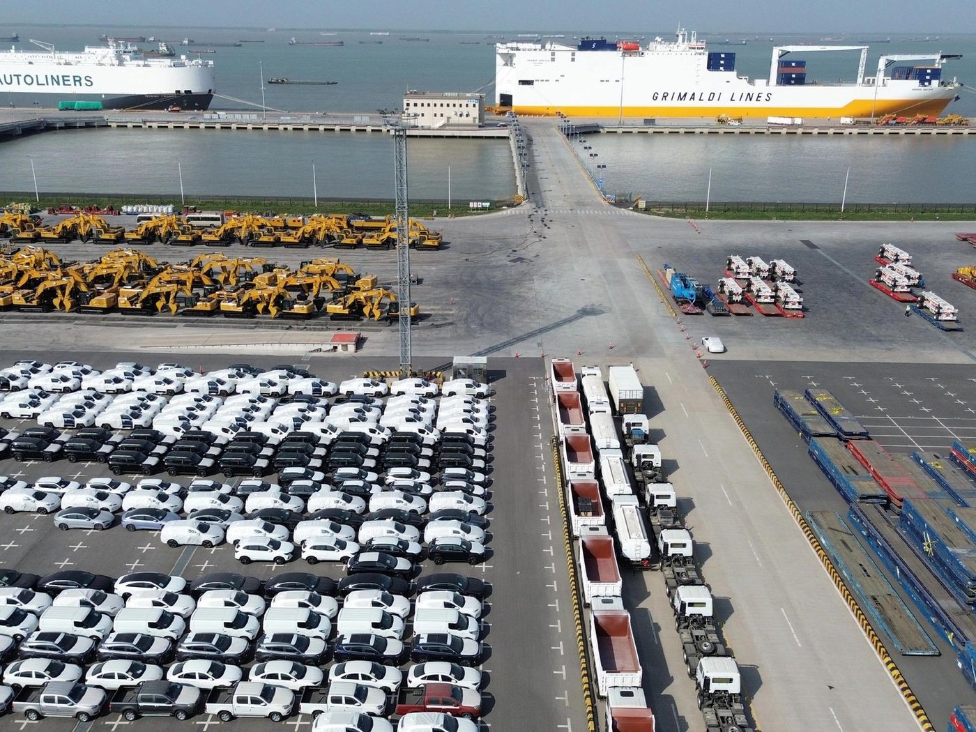 Aerial view of an export yard with new vehicles and an excavator alongside a vehicle carrier at berth