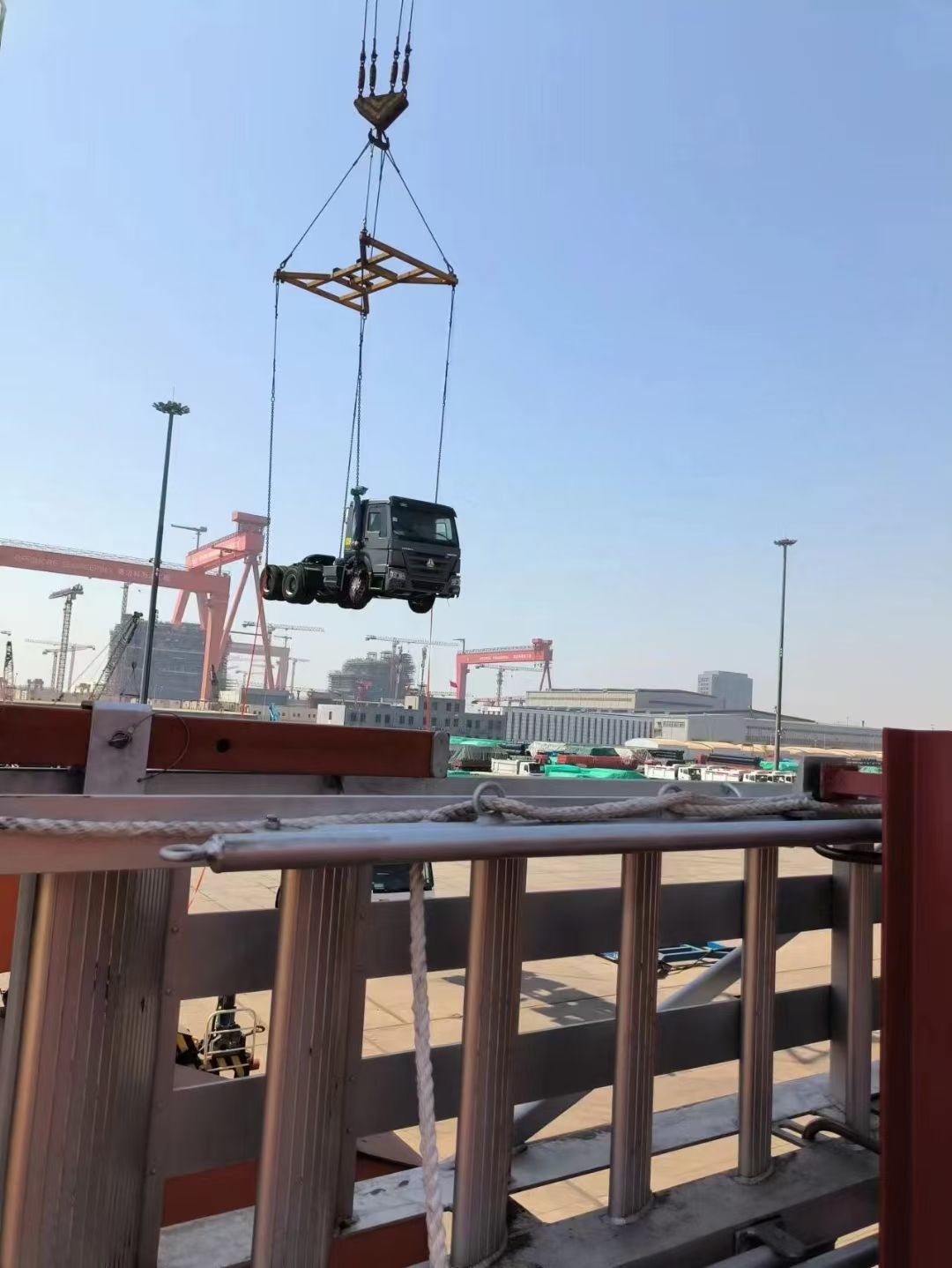A truck tractor head lowered to the vessel deck by crane, guided by tag lines from the loading gang